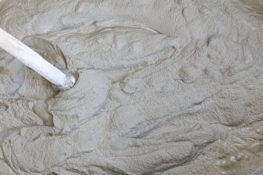 İnşaat işleri için gri ıslak çimento dokusunun karıştırıldığını, yüzeyde kabataslak kalıp oluşturulduğunu ve çerçeve içerisinde inşaatçı aracının görülebildiğini göster