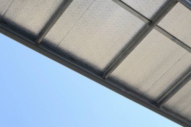 Metal çerçeve yapısı ile şeffaf beyaz çatı tepe örtüsünün altında sakin mavi gökyüzü arkaplanına karşı inşaat detaylarını ve minimal mimari tasarımı gösteren görünüm