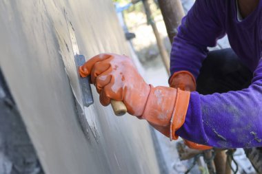 Turuncu koruyucu eldiven giyen inşaat işçisi küreği kullanarak gri beton duvarı odaklı, gayretli profesyonel bina yenileme projesiyle kaplıyor.