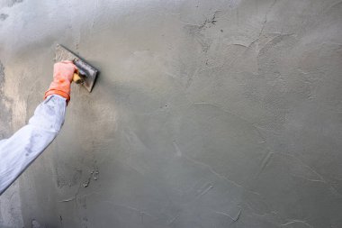 Profesyonel inşaatçı gri beton duvarı yenileme için malayla kaplıyor, endüstriyel konut geliştirme sahasında kaba beton yüzey üzerine elle inşa çalışmalarına odaklandığını ve kendini adadığını gösteriyor.