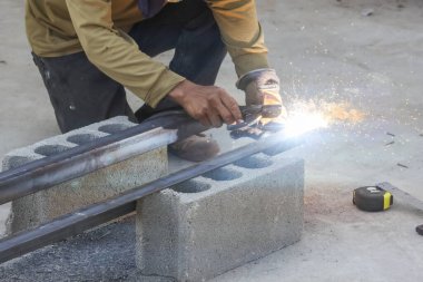 Tehlikeli endüstriyel atölye inşaatında parlak kıvılcımlar ve parıltılar saçan demir boruları kesmek için çok çalışan ciddi bir kaynakçı.