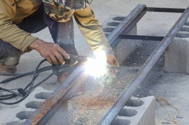 Kaliteli endüstriyel işçiler çelik çerçeve yapısını yoğun bir odak ve kararlılıkla korumacı ekipmanlar kullanarak parlak kıvılcımlar ve ışık saçar.