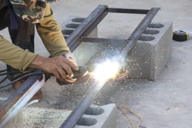 İnşaat sırasında parlak kıvılcımlar saçan metal çerçeveyi kesen usta işçiler açık alanda odaklanmış ve çalışkan bir atmosfer yaratıyor.