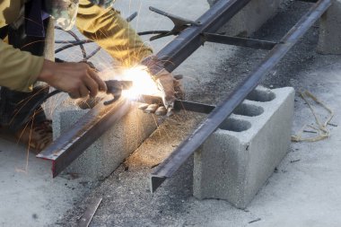 Odaklanmış kaynakçı, yoğun inşaat sahasında özen ve konsantrasyon gerektiren parlak kıvılcım ile beton blokta metal çerçeveye katılan araçla çok çalışıyor.