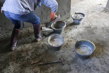 Çalışkan inşaat işçisi inşaat alanında harç alçısını karıştırırken mala ve kovayı yenileme projesi için gün boyunca özenli bir odak ve enerjik çabayla kullanıyor.