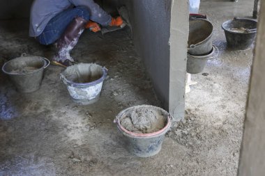İnşaat işçisi bacakları, ıslak beton inşaat sahasında plastik kovaya çimento karıştırarak endüstriyel yenileme işinde ağır işçilik yaptığını gösteren botlar giyer.
