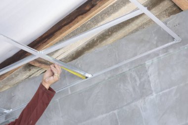 Profesyonel işçi el, tavan yenileme inşaat alanı için askıya alınmış metal çerçeve şebekesi kuruyor, hassasiyet ve iyileştirmeye odaklanıyor