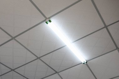 Beyaz damlalar üzerinde parlayan tek bir floresan boru ışığı ofis veya hastane odasındaki steril atmosferi gösteriyor.