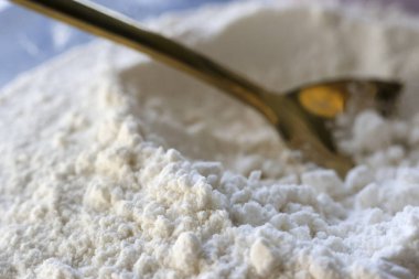 Beyaz, yumuşak un dokusunu, ev yapımı pişirmeye hazırlanan altın kaşıkla yakından görmek mutfak atmosferinde sıcak ve nazik bir his yaratıyor.