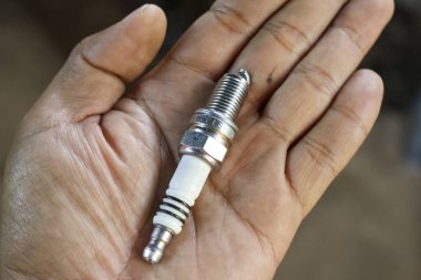 Tamirci elinde yeni bir buji tutuyor. Tamir ve bakım işleri için gerekli otomotiv parçası. Kurulumdan önce ekipman görünümünü kapat