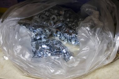 Parlak galvanizli çelik kanat fındık bağlayıcılarıyla dolu plastik poşeti temizleyin. İnşaat, montaj ve onarım için endüstriyel donanım yığınının görüntüsünü kapat