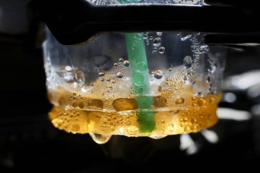Plastik bardakta yeşil pipetli soğuk içecek dramatik bir şekilde yakın plan. Yoğunlaşması ve kabarcığı ile kahverengi sıvı içecek tek damla düşerken ferahlatıcı bir an yaratır