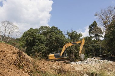 İnşaat alanında güçlü bir sarı kazıcı, dünyayı eşeliyor. Bu sahne, orman çevresinin yıkımını gösteren endüstriyel gelişimi ve ormansızlaşmayı resmediyor.