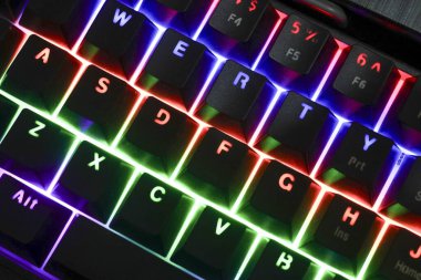 Renkli RGB arka aydınlatma tuşlarıyla klavyeyi kapat. Modern bilgisayar teknolojisi ekipmanları heyecan verici bir ruh hali için karanlık odada parlak neon ışıklarla parıldıyor.