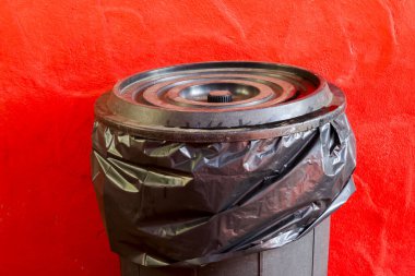 Çöp kutusunun içindeki siyah plastik çöp torbası ya da çöp kovası. Sade, canlı kırmızı arkaplan kavramına karşı çöp için izole edilmiş bir konteynır