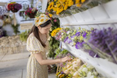 Eski moda elbiseli hoş bir Asyalı kadın çiçekçi dükkanındaki raftan taze çiçek buketini incelikle seçiyor. Mutlu ve sakin yaşam tarzı anı