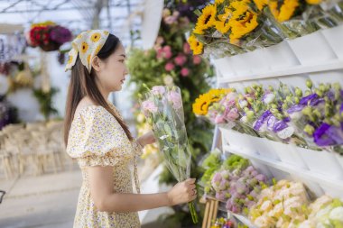 Çiçekçide güzel bir buket seçen mutlu genç Asyalı kadın. Düşünceli bayan müşteri özel durumlar için yerel marketten taze çiçek alıyor.