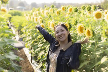 Güzel ayçiçeği tarlasında gülümseyen mutlu Asyalı kadın. Doğanın ve yazın tadını çıkaran neşeli insan, kırsalda özgür ve neşeli hissediyor.