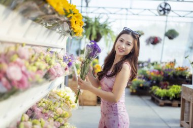 Çiçek buketi almak için çiçek almaya giden mutlu bir kadın. Bahçe merkezinde taze çiçekleri seçen güzel bir insan, neşeli bir yaşam tarzının keyfini çıkarıyor.