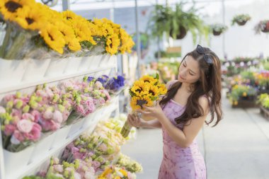 Mutlu Asyalı kadın alışverişi, parlak çiçekçiden taze ayçiçeği buketi seçiyor. Bahçe merkezinden güzel bitkiler seçmek keyifli bir an.