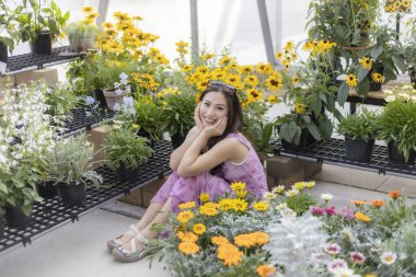 Güzel renkli çiçek ve bitkilerle çevrili, parlak seranın zemininde oturan mutlu genç kadın. Bahçe merkezinde ya da çocuk odasında doğanın tadını çıkaran memnun bir kadın.