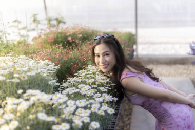 Güzel çiçek bahçesinde gülümseyen mor elbiseli mutlu genç Asyalı kadın. Doğanın ve bahar mevsiminin tadını çıkaran sakin bir insan portresi.