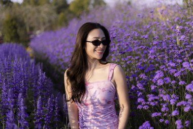 Mor Margaret çiçek tarlasında gülümseyen uzun saçlı mutlu Asyalı bir kadının huzurlu portresi. Güneşli bir yaz gününde doğanın tadını çıkaran biri.