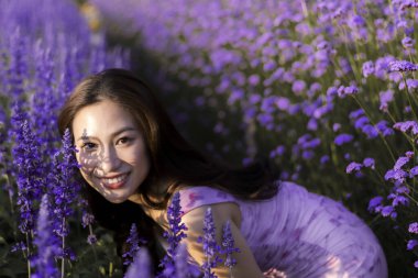 Mor lavanta tarlasında gülümseyen mutlu genç Asyalı kadın. Bu güzel kız yaz günü açık havada doğanın aromasını ve güzelliğini seviyor.