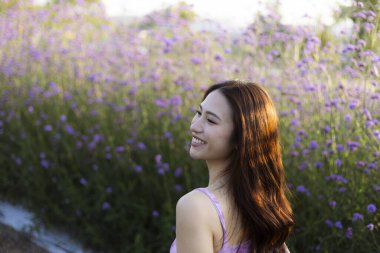 Mor çiçek tarlasında mutlu bir şekilde gülümseyen uzun saçlı güzel Asyalı kadın. Doğanın ve yazın tadını çıkaran, dingin hisseden bir kadının neşeli portresi.