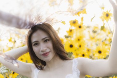 Sarı ayçiçeği tarlasında yaz güneşinin tadını çıkaran mutlu Asyalı kadın. Güzel genç bayan model portresi doğada rüya gibi arka planı var.