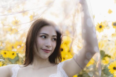 Yaz boyunca ayçiçeği tarlasında güzel mutlu Asyalı kadın portresi. Saf kumaşı sıcak güneş ışığında tutan genç bir kadın. Nazik ve dingin bir ruh hali içinde.