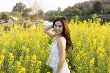 Mutlu gülümseyen kadın güzel bir yaz gününün tadını çıkarır. Sarı çiçekli bu açık hava portresi doğanın güzelliğini ve kaygısız neşe hissini yakalar.