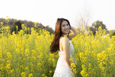 Sarı çiçek tarlasında mutlu Asyalı kadın yaz boyunca doğanın tadını çıkarıyor. Kırsal kesimde neşeyle gülümseyen genç bir bayanın güzel portresi.