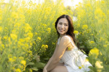 Sarı çiçek tarlasında sevinçle gülümseyen mutlu Asyalı kadın. Güneşli bir yaz gününde doğanın güzelliğini kutlayan sakin bir manzara.