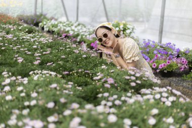 Güneş gözlüklü mutlu genç kadın bahçe serasının içinde güzel doğanın tadını çıkarıyor. Güzel bir yaz günü. Çiçek kokulu. Bahçeyle ilgili çiçeklerle çevrili.