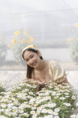Güzel mutlu Asyalı kadın, portrede güzel bir gülümseme. Çiçek bahçesinde doğanın tadını çıkaran genç insan hoş bir bahar günü beyaz papatya çiçekleriyle dolu.