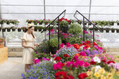 Çiçek almak için çiçekçiye giden mutlu genç bir kadın. Bahçe işleriyle ilgili neşeli bir an Parlak seranın içinde Güzel bir bahar günü
