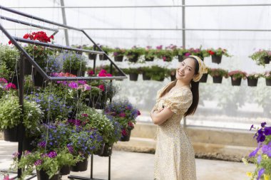 Serada bahçıvanlık yaparken gülümseyen mutlu genç bir kadın. Etrafı güzel çiçek ve bitki örtüsüyle çevrili, botanik yapmaktan hoşlanıyor.