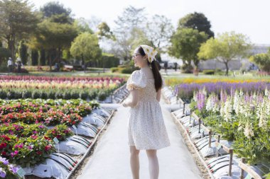 Güzel Asyalı genç bir kadın huzurlu çiçek bahçesinde yürüyor. Kamu parkındaki bu huzurlu açık hava sahnesi ilkbaharda doğada neşe ve özgürlüğü yansıtıyor.