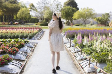 Baharda güzel çiçek bahçesinde yürüyen mutlu genç Asyalı kadın. Huzurlu seyahat deneyimi rengarenk çiçeklerin tadını çıkarıyor ve tatilde hayat dolu doğanın tadını çıkarıyor.