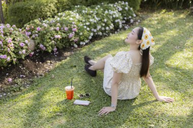 Serene mutlu genç kadın yaz boyunca parkta ya da bahçede yeşil çimlerde dinleniyor. Güzel bir insan serin bir içecekle huzurlu bir hayat sürüyor.