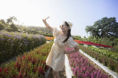 Renkli çiçek bahçesinde yaz yolculuğunun tadını çıkaran mutlu, güzel genç bir kadın. Doğadaki neşeli insan güneşin altında neşe, açık havada canlı bir yaşam tarzı hissediyor.