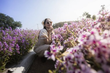 Mor çiçek tarlasında düşünceli yaşlı kadın güneşli günün tadını çıkarıyor. Bu barışçıl yetişkin güzel bir bahçede oturuyor, mutlu ve doğal güzellikte rahatlamış hissediyor.