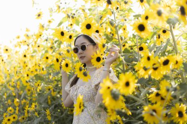 Güzel genç bir kadın yaz boyunca ayçiçeği tarlasında huzurlu bir mutluluk hissediyor. Bu portre, doğada sarı çiçeklerle çevrili huzurlu bir anı yakalar.