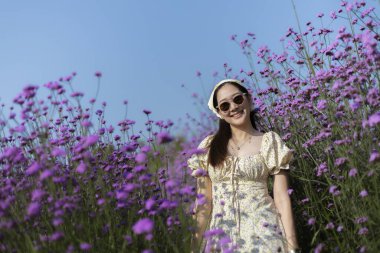 Güzel mor çiçek tarlasında gülümseyen mutlu genç Asyalı kadın. Açık mavi gökyüzü ile yaz tatilinin tadını çıkaran kişinin yaşam tarzı portresi
