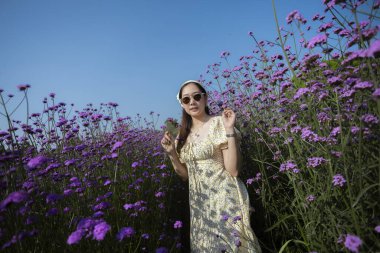 Yazlık elbiseler içinde mutlu güzel bir kadın huzurlu bir günün tadını çıkarıyor. Güzel seyahat portresi canlı mor bir çiçek tarlasında duruyor doğa ve berrak mavi gökyüzü