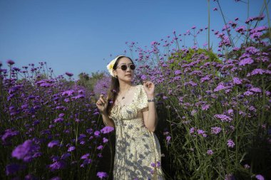 Mor çiçek tarlasında güneşli günün tadını çıkaran mutlu güzel kadın. Canlı doğa ve mavi gökyüzü ile çevrili zarif bir bayanın huzurlu hayat tarzı seyahat portresi.