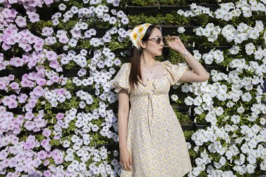 Açık hava çiçek bahçesinde poz veren sakin ve güzel bir kadın. Bu portre onun renkli çiçeklere karşı düşünceli yüz ifadesini yansıtıyor.