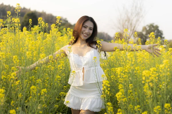 Yaz boyunca sarı çiçek tarlasında mutluluk ve özgürlükle gülümseyen mutlu Asyalı genç kadın. Doğanın tadını çıkaran, kaygısız ve güneşin altında mutlu bir yetişkin.