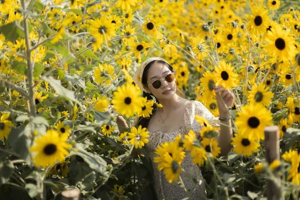 Ayçiçeği tarlasında gülümseyen güzel Asyalı kadın. Doğada yazın tadını çıkaran neşeli insan, sarı çiçekli güzel bir portre için dışarıda poz veriyor.